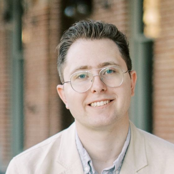 Justin S. Severn, smiling, in glasses and a light linen jacket in front of a brick building.